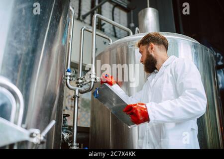 Caucasian male  technologist expert in white suit  operating production machine in food factory and doing quality control and holding checklist Stock Photo