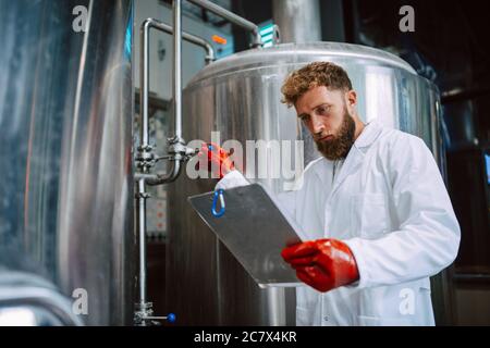 Caucasian male  technologist expert in white suit  operating production machine in food factory and doing quality control and holding checklist Stock Photo