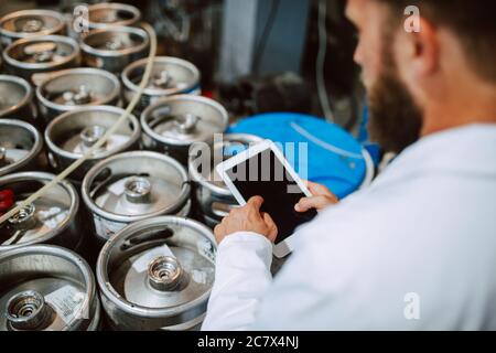 Closeup of tablet computer in hand of professional caucasian technologist expert in white uniform  in production plant - food or drink factory Stock Photo