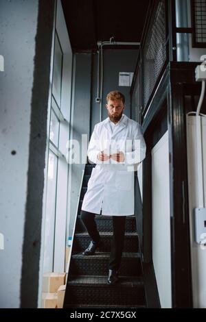 Professional caucasian technologist expert  in white uniform stands on steps in production plant - factory Stock Photo