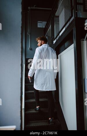 Professional caucasian technologist expert in white uniform stands on steps in production plant - factory Stock Photo