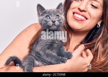 Young beautiful latin woman smilling happy. Standing with smile on face holding adorable cat over isolated white backgroun Stock Photo