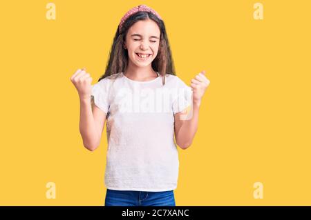 Cute hispanic child girl wearing casual white tshirt very happy and excited doing winner gesture with arms raised, smiling and screaming for success. Stock Photo