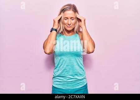 Middle age caucasian blonde woman wearing sports clothes over pink background with hand on head for pain in head because stress. suffering migraine. Stock Photo