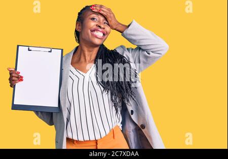 Young african american woman wearing business clothes holding clipboard stressed and frustrated with hand on head, surprised and angry face Stock Photo