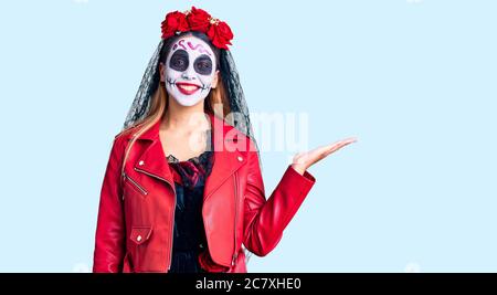 Woman wearing day of the dead costume over background smiling cheerful presenting and pointing with palm of hand looking at the camera. Stock Photo