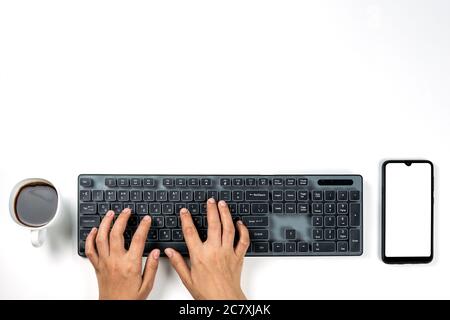 Office worker at work in early morning. Cup of black coffee, mobile phone with empty screen and person typing on pc keyboard Stock Photo