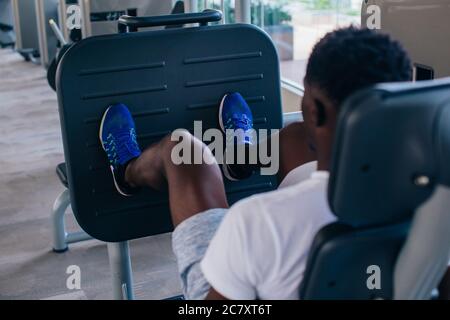 Back view of African American man doing exercise on leg press during fitness training in modern gym. Stock Photo