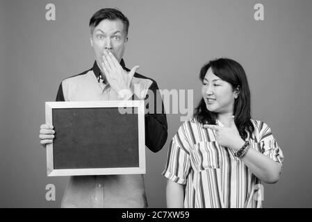 Portrait of young handsome businessman and mature Asian businesswoman together with blackboard Stock Photo