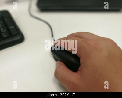 Closeup shot of a male hand holding a computer mouse next to a black keyboard Stock Photo