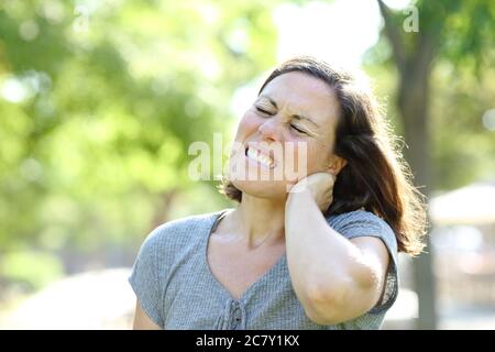 Adult woman in pain suffering neck achestanding in the park at summer Stock Photo