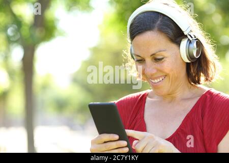 Happy adult woman listening music on smart phone with headphones in a park Stock Photo
