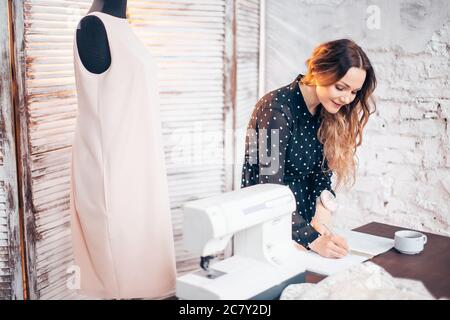 tailor writing in notebook at workspace with sewing machine and tailoring items Stock Photo
