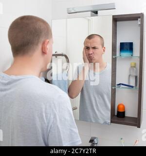 hangover concept - tired or sleepy man looking at mirror in bathroom Stock Photo