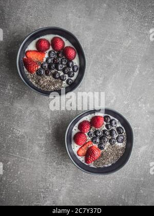 Two blue bowls with yoghurt and fruits on grey concrete background. Stock Photo