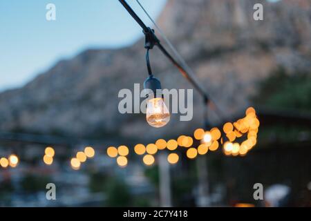 A garland of incandescent light bulbs, in the evening, against the backdrop of bokeh. Stock Photo