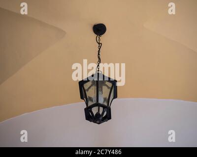 Electric black vintage lamp or lantern hanging on a chain under a vaulted yellow and white ceiling. Copy space Stock Photo