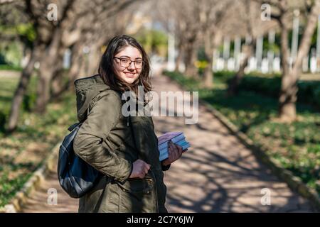 Intellectual young girl stays and look to someone in a park with some books in her hands. High quality photo Stock Photo