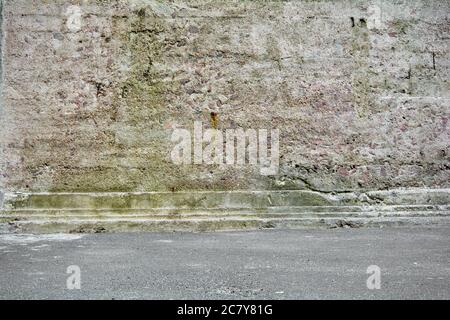 Grunge city background with mossy old stone wall with concrete molding and asphalt Stock Photo