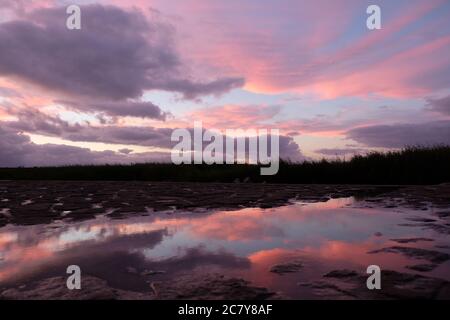 colorful sunset clouds sky and reflection in puddle water. Low angle Stock Photo