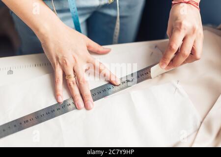 Close up. hands woman Tailor working cutting a roll of fabric on which she has marked out the pattern of the garment she is making with tailors chalk. Stock Photo
