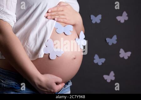 pregnant woman's belly with paper colorful butterflies over grey background Stock Photo