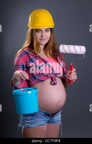 happy young beautiful pregnant woman in helmet with builder's tools over grey background Stock Photo