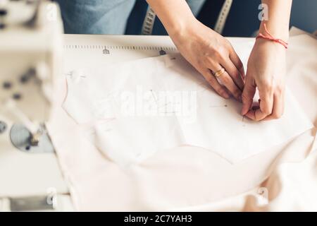 Close up. hands woman Tailor working cutting a roll of fabric on which she has marked out the pattern of the garment she is making with tailors chalk. Stock Photo