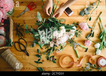 hands of florist against desktop with working tools and ribbons on wooden background Stock Photo