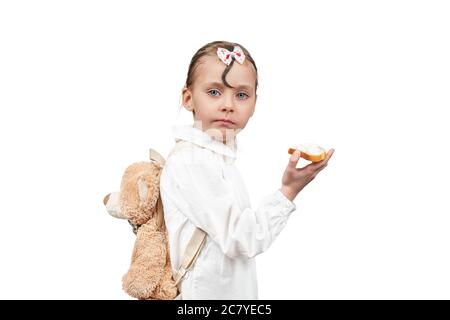 Portrait of a beautiful little stylish girl with a backpack behind her back and with a sandwich in her hand, isolated on white background Stock Photo