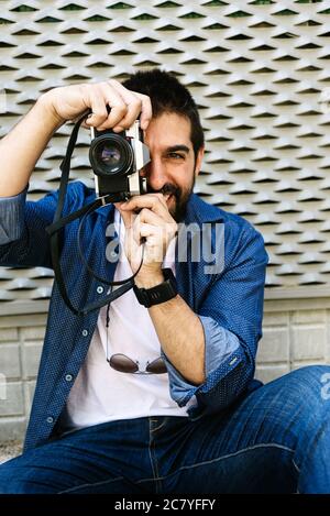 Cheerful bearded traveler man sitting on ground while using checking a camera Stock Photo