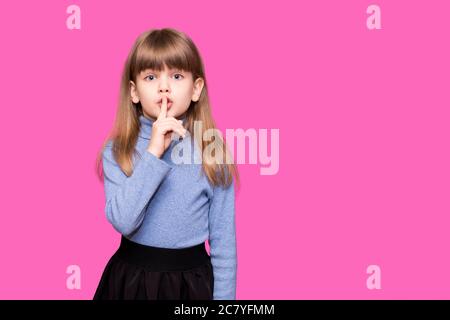 Emotional child girl has secret. Little girl with wonder face keeps finger on lips, shows silence sign, asks to be quiet and stop make loud noise isol Stock Photo