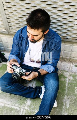 Cheerful bearded traveler man sitting on ground while using checking a camera Stock Photo