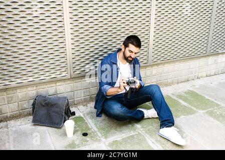 Cheerful bearded traveler man sitting on ground while using checking a camera Stock Photo