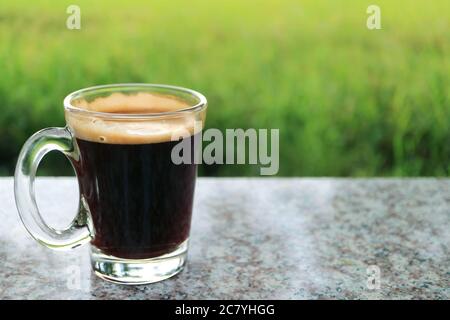One Hot Black Coffee in a Transparent Glass with Blurry Green Meadow in Background Stock Photo