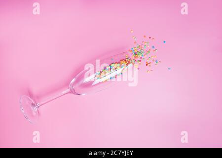 Cake confetti decorations in the champagne glass on pink background. Stock Photo