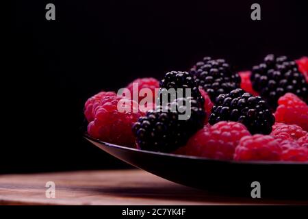 Blackberries and raspberries fruits composition on a black plate and black background. Fresh and tasty looking organic food for vegan in a summer seas Stock Photo