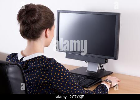 back view of young beautiful business woman in office using computer with empty monitor screen Stock Photo