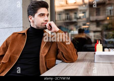 Young attractive casual man thoughtfully looking aside in cafe on city street Stock Photo