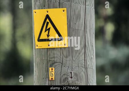 Electricity warning sign on old wooden pole. Stock Photo