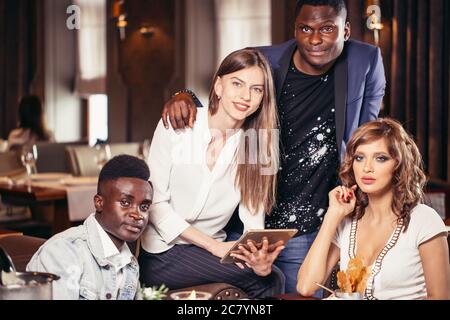 Group of young travellers having a good time at restaurant choosing best root for vacation trip, looking at camera Stock Photo