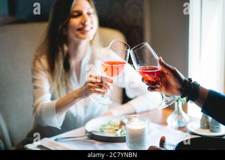 Mixed-race young couple toasting with glasses of wine at cafe Woman in focus. Stock Photo