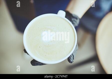 Barista wearing medical latex black gloves, making cappuccino, bartender preparing coffee drink. Blurred image, selective focus Stock Photo