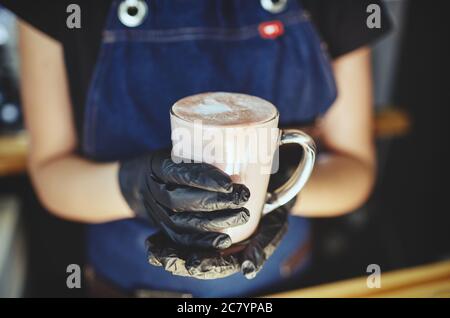 Barista wearing medical latex black gloves, making pink matcha latte with milk.Bartender preparing tasty drink Stock Photo