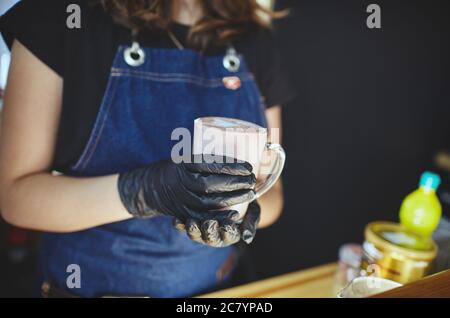 Barista wearing medical latex black gloves, making pink matcha latte with milk.Bartender preparing tasty drink Stock Photo