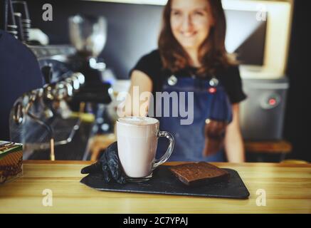 Barista wearing medical latex black gloves, making pink matcha latte with milk. Bartender preparing tasty drink and brownie cake Stock Photo
