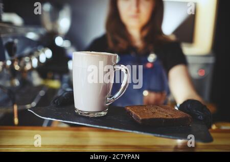 Barista wearing medical latex black gloves, making pink matcha latte with milk. Bartender preparing tasty drink and brownie cake Stock Photo