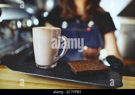 Barista wearing medical latex black gloves, making pink matcha latte with milk. Bartender preparing tasty drink and brownie cake Stock Photo