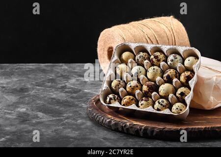 Quail eggs in a gray cardboard box. Close-up photo. Black concrete background. Healthy protein foods. Small speckled eggs for breakfast Stock Photo