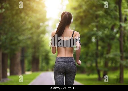 Back View Of Sporty Fit Young Woman Jogging In Green City Park